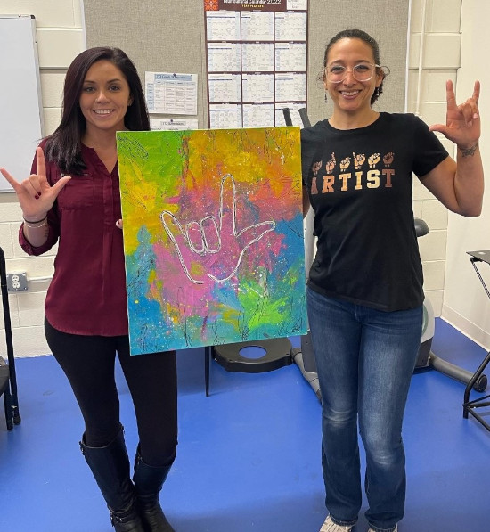 Two members holding up their painting from ASL paint night event