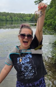 Transitions member at a pond proudly holding up something she found